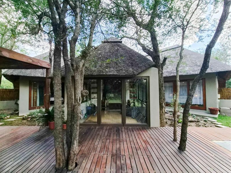 Rear view of a house featuring a thatched roof, timber decking, and large sliding glass doors opening onto the outdoor space.