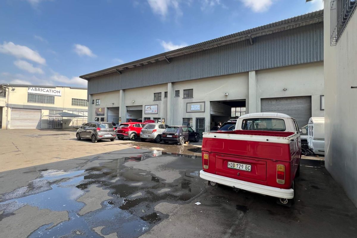 Exterior view of an industrial office and warehouse facility featuring multiple roller shutter access points and a paved yard area.