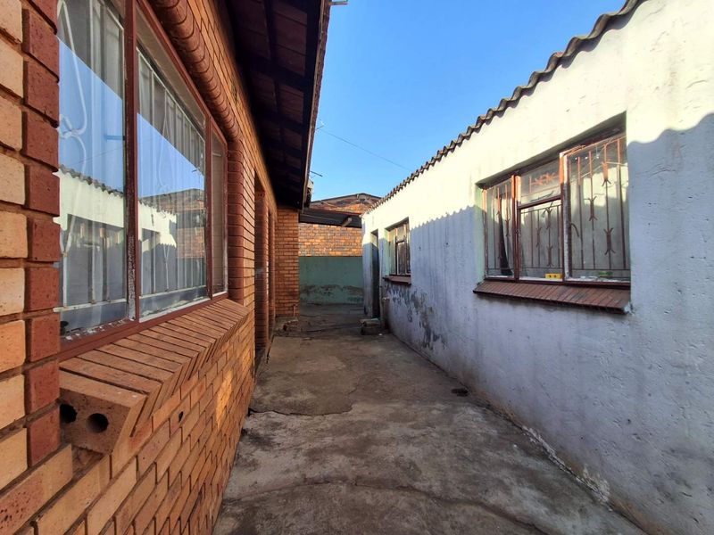 A narrow exterior side passage between two brick structures featuring concrete paving and security-barred windows.