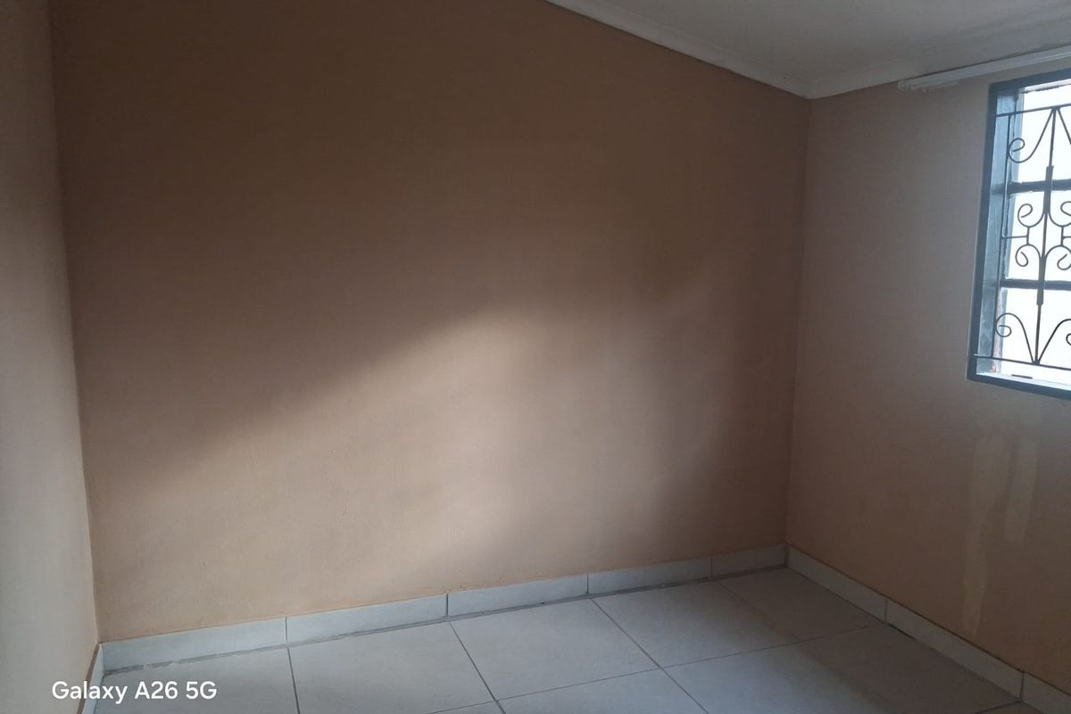 An empty bedroom featuring tiled flooring and a window with security burglar bars, requiring minor cosmetic updates to the wall finishes.