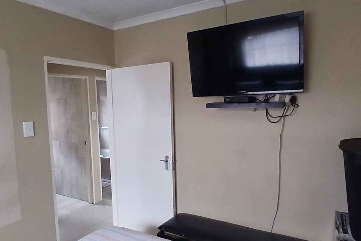 A bedroom featuring a wall-mounted television and direct access to an adjacent bathroom, showing signs of wear on the ceiling.