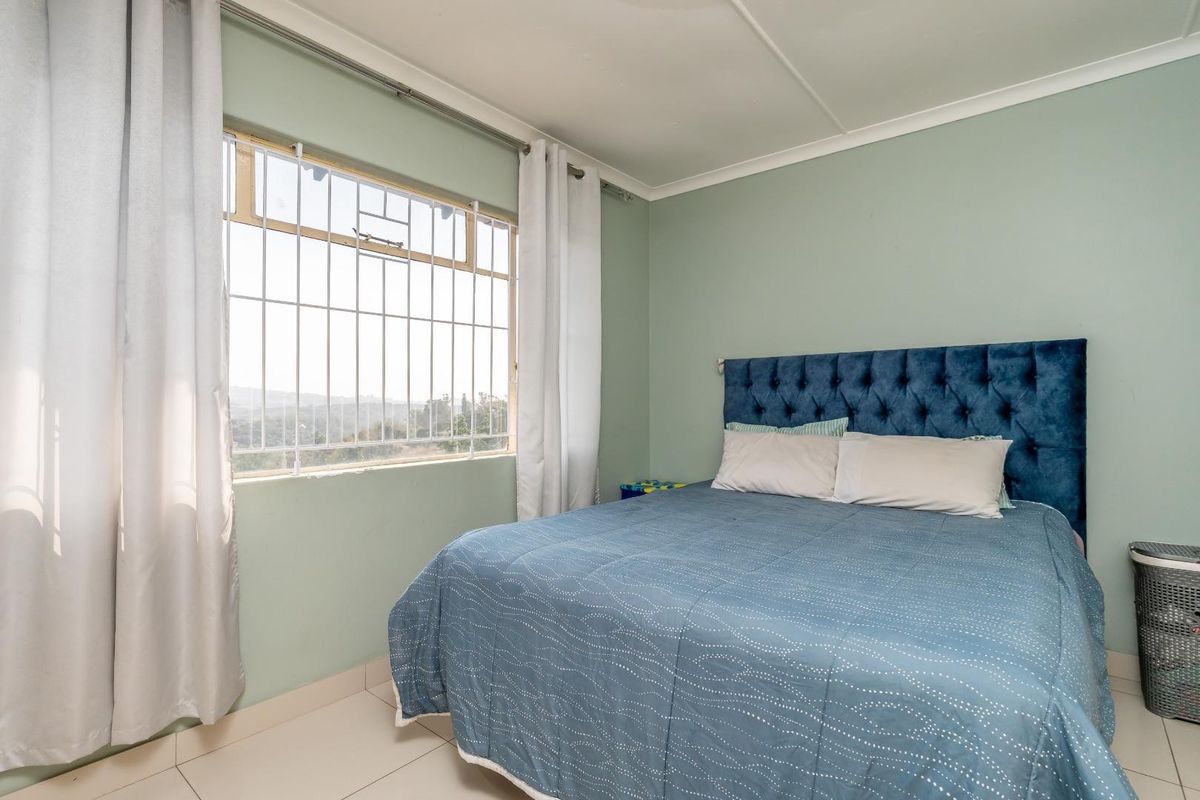 A bedroom featuring tiled flooring, light green walls, and a window fitted with security bars, offering a functional and well-lit living space.