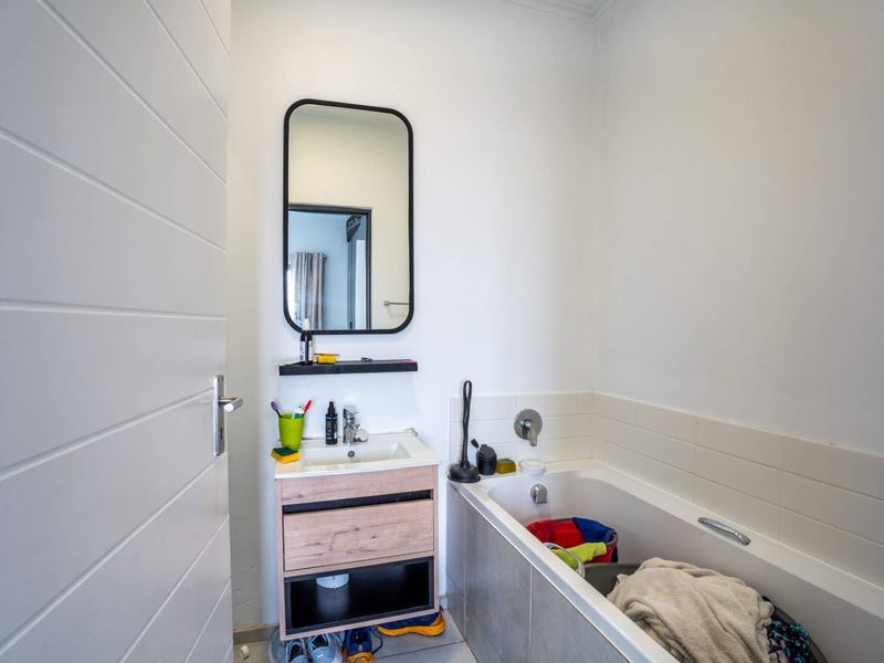 A functional bathroom featuring a modern wood-finish vanity, basin, wall-mounted mirror, and a bathtub with tiled surround.