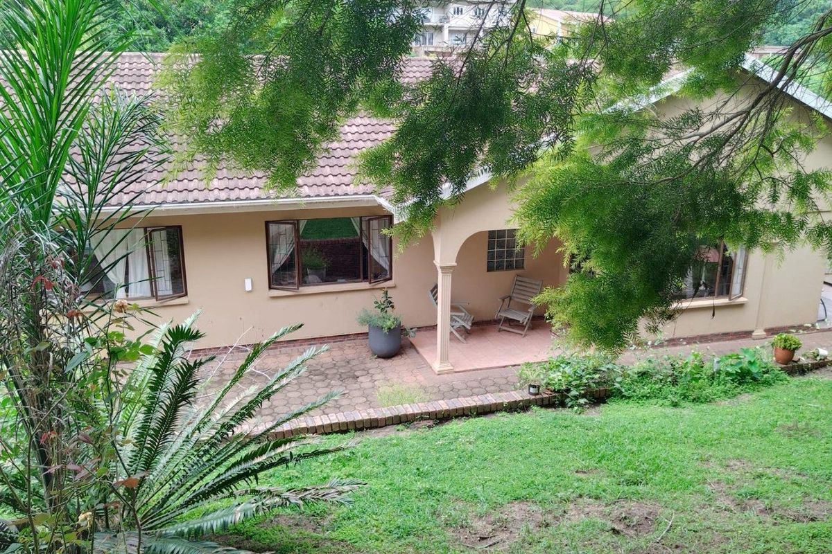 Rear view of the house featuring a covered patio area, tiled roof, and paved outdoor space overlooking the garden.