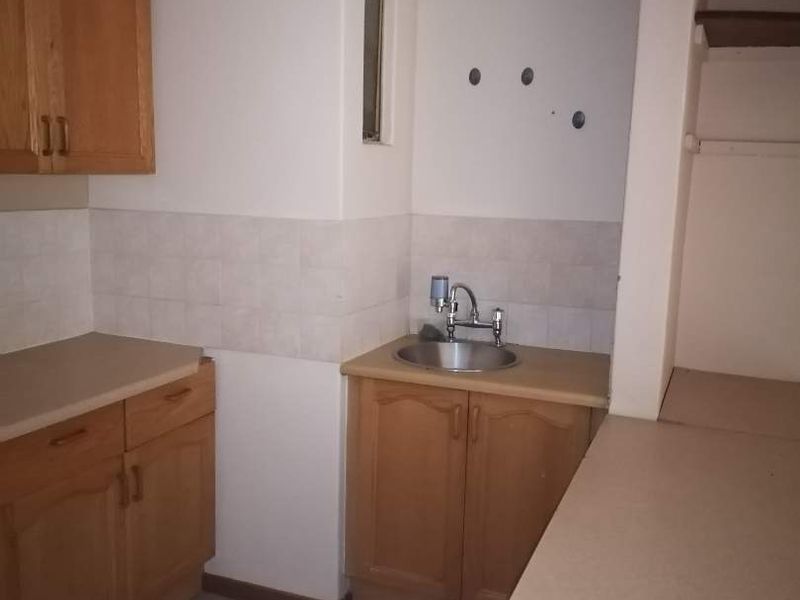 A dated kitchen area featuring wooden cabinetry, laminate countertops, and a stainless steel sink, currently vacant and ready for renovation.