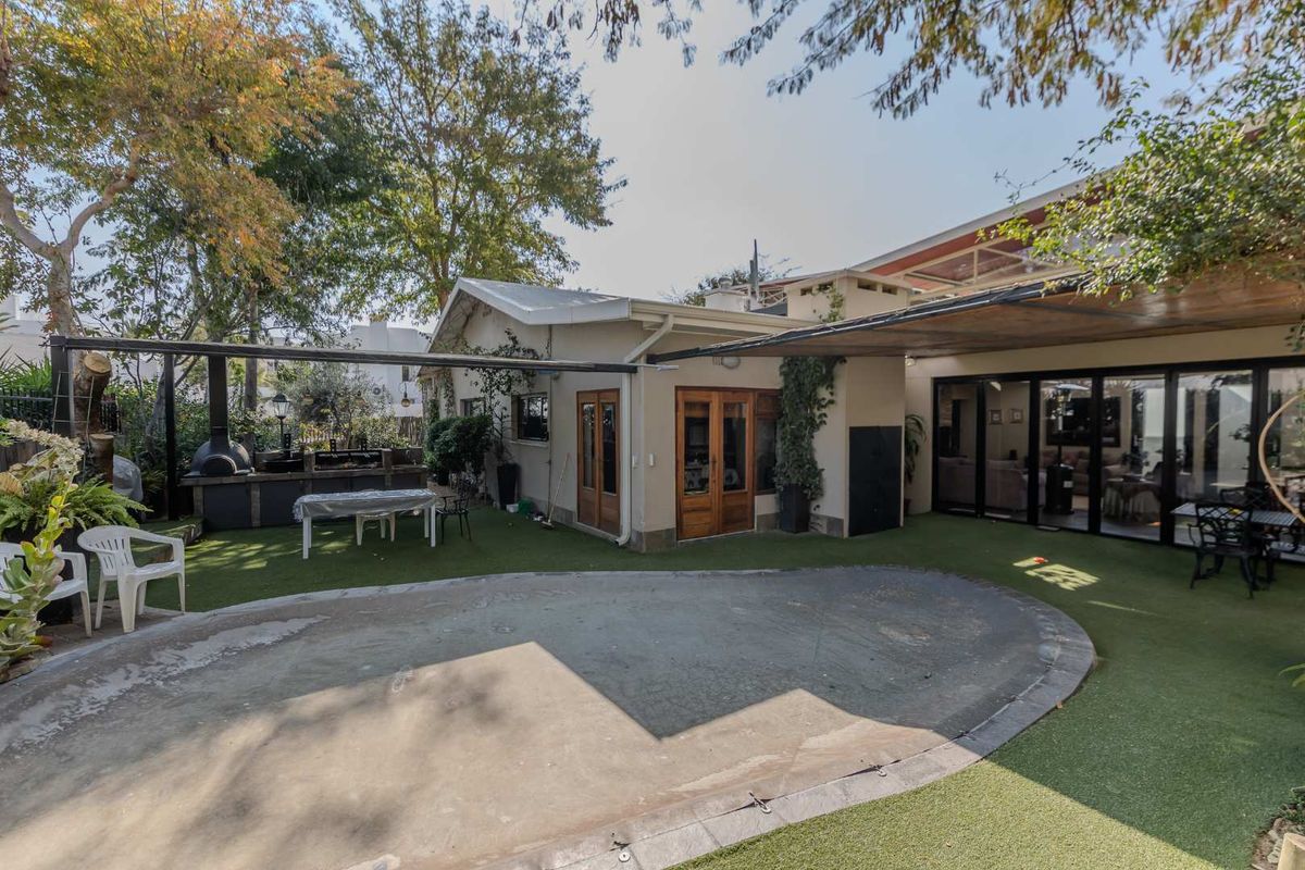 Rear exterior view featuring a covered patio area, built-in braai, and artificial lawn space with direct access to the home via sliding glass doors.