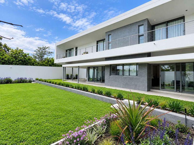 Modern two-story residence featuring a spacious rear garden, covered patio, and an expansive upper-level balcony with sleek stainless steel balustrades.