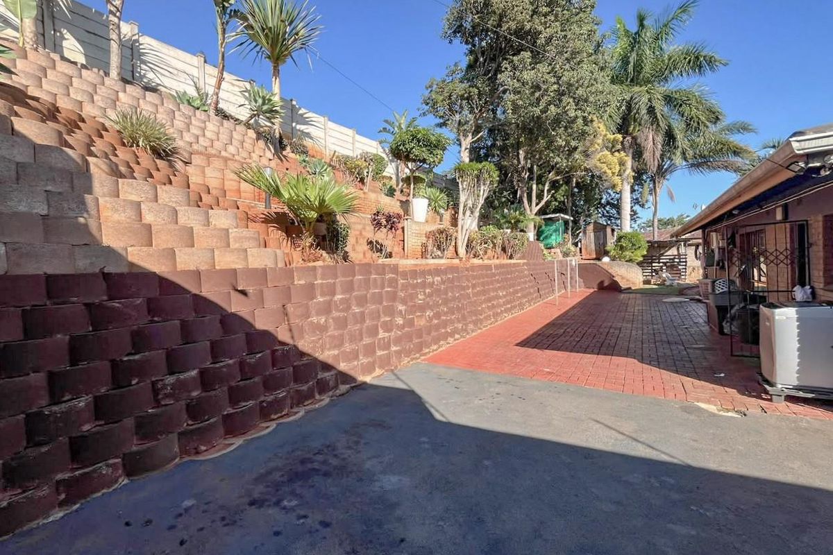 A multi-level terraced garden featuring extensive concrete block retaining walls, paved walkways, and established trees alongside the rear of the property.