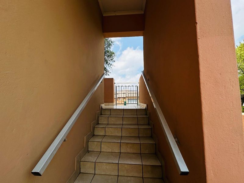An exterior staircase entrance featuring tiled steps, metal handrails, and a security gate leading to the apartment access point.