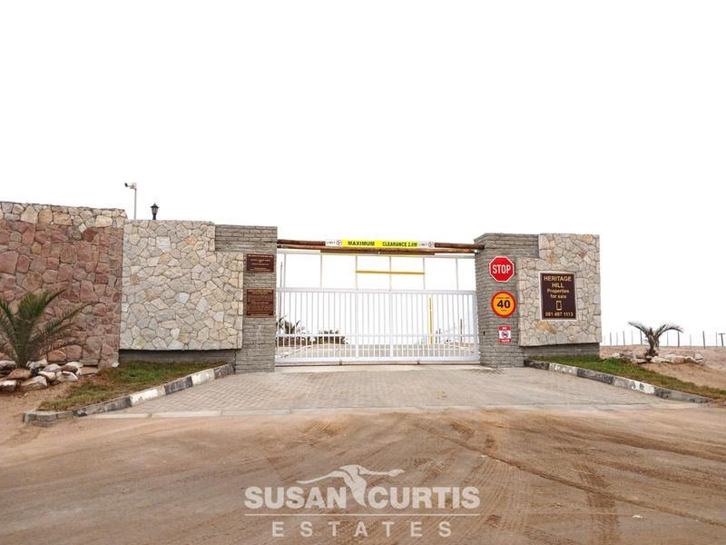 A secure gated entrance to the residential estate featuring stone-clad pillars, a white metal security gate, and paved driveway access.