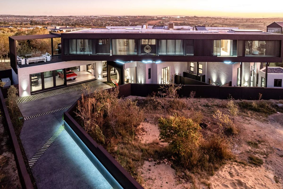 Aerial view of a contemporary luxury residence featuring a modern facade, integrated garage, extensive exterior lighting, and a paved driveway at dusk.
