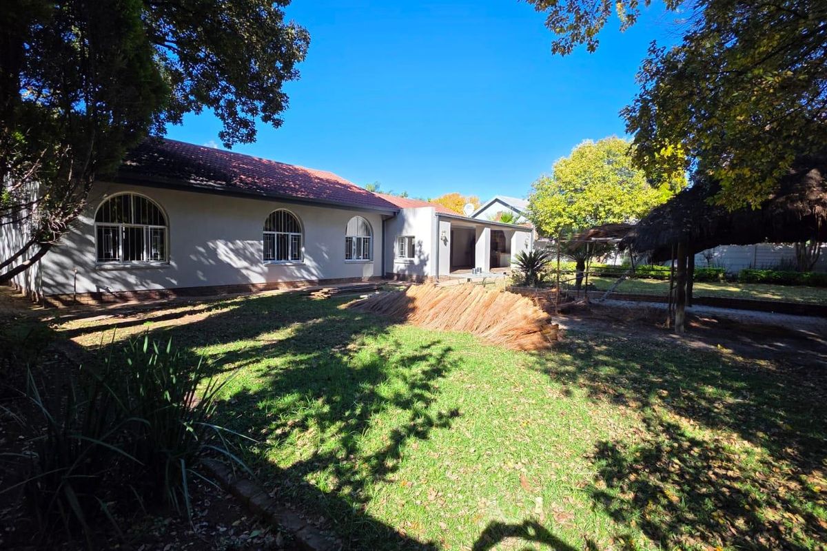 Rear view of the property featuring a spacious garden, a covered patio area, and a traditional thatched lapa structure.