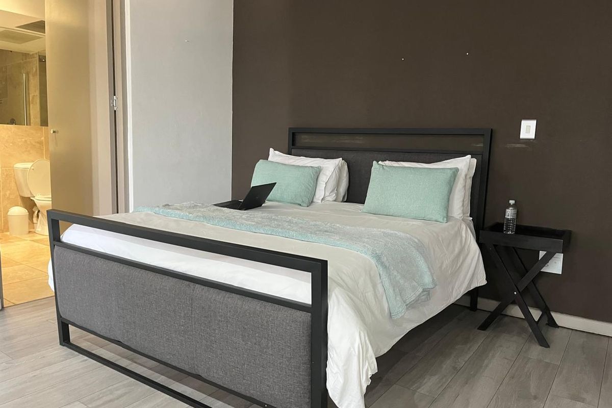 A bedroom featuring wood-look laminate flooring and a dark accent wall, with an adjoining en-suite bathroom visible in the background.
