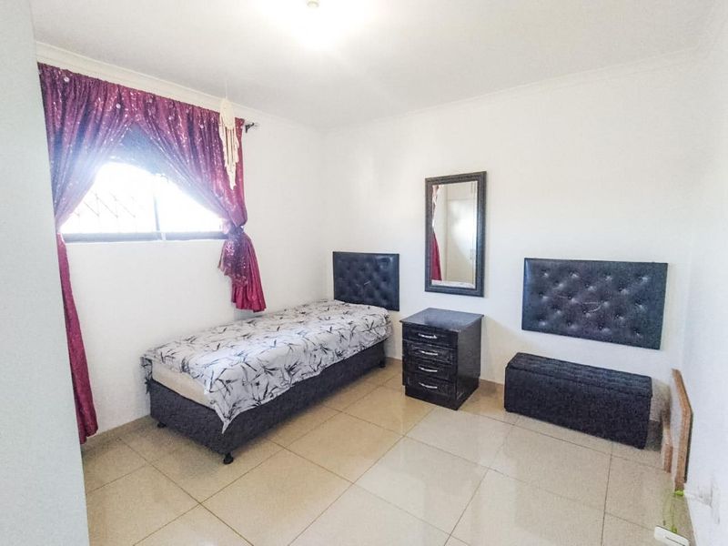 A bedroom featuring neutral tiled flooring and a window fitted with security bars.
