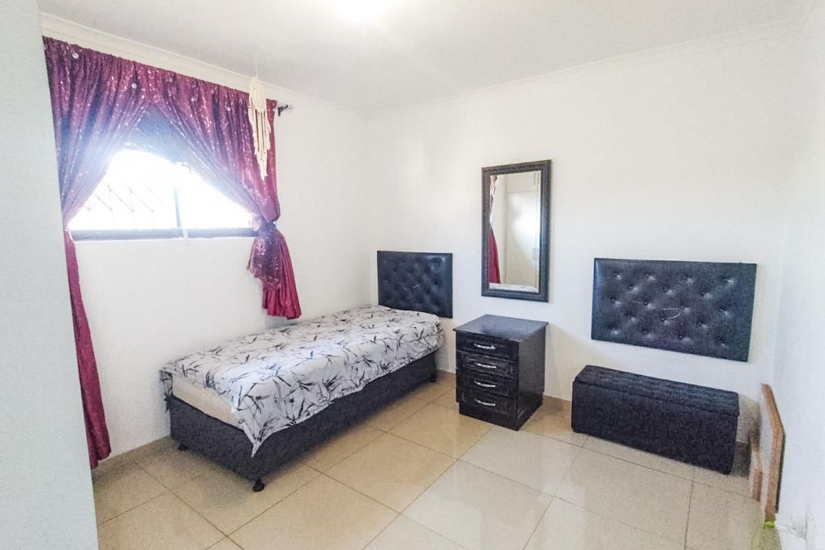 A bedroom featuring neutral tiled flooring and a window fitted with security bars.