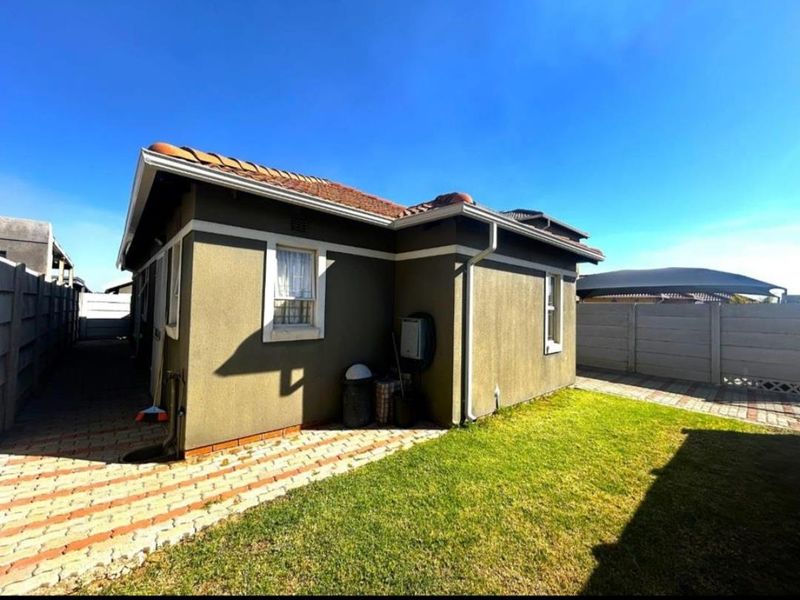 Rear exterior view of the house featuring a tiled roof, paved walkway, and a small lawn enclosed by a precast concrete boundary wall.