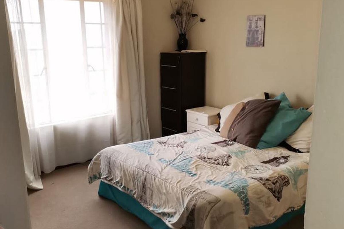 A standard bedroom featuring neutral wall tones, carpeted flooring, and a large window allowing for natural light.