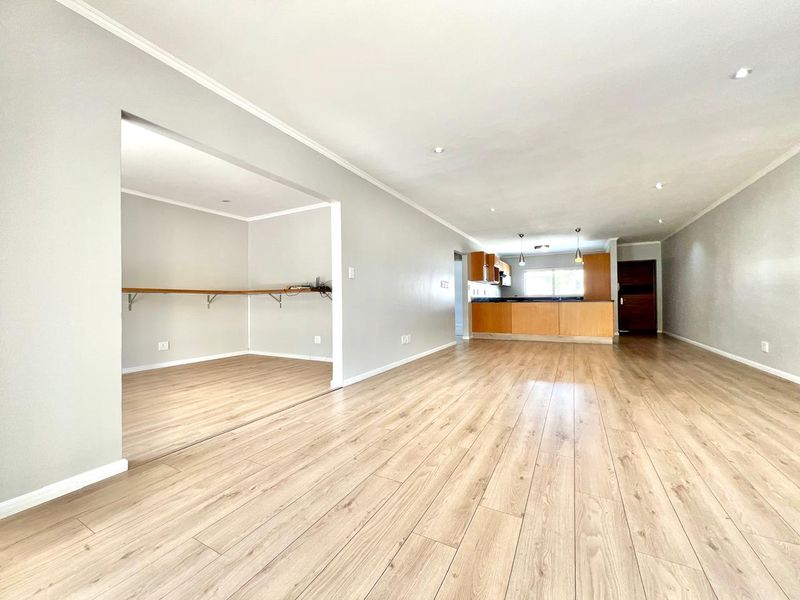 Spacious open-plan living area featuring light laminate flooring, recessed lighting, and a functional kitchen with wooden cabinetry and a breakfast bar.