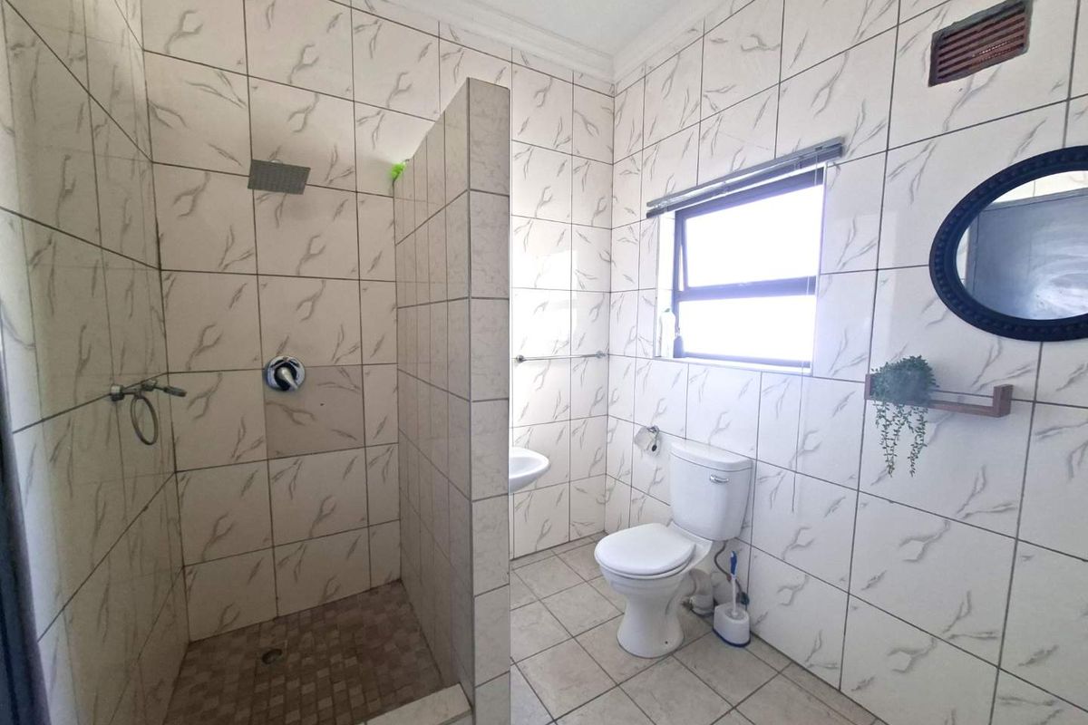A functional bathroom featuring a walk-in shower with a partition wall, a standard toilet, and a wall-mounted basin with tiled walls and flooring.