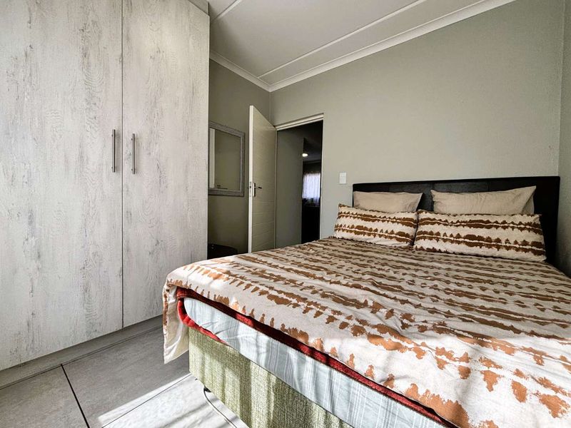 A well-maintained bedroom featuring neutral wall tones, tiled flooring, and a large built-in wardrobe with a modern wood-grain finish.