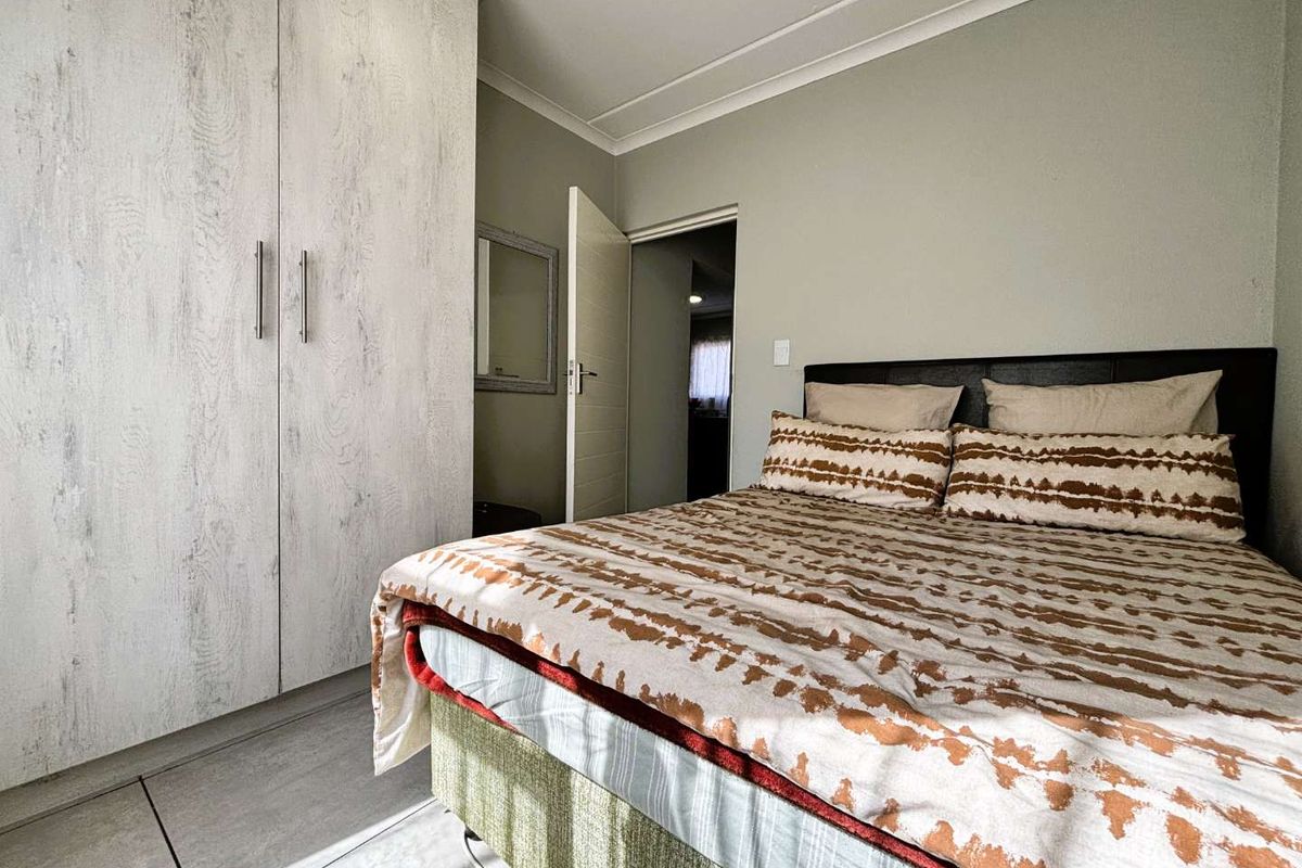 A well-maintained bedroom featuring neutral wall tones, tiled flooring, and a large built-in wardrobe with a modern wood-grain finish.