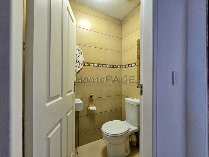 A compact guest bathroom featuring neutral ceramic wall and floor tiles, a standard toilet, and a small wall-mounted basin.