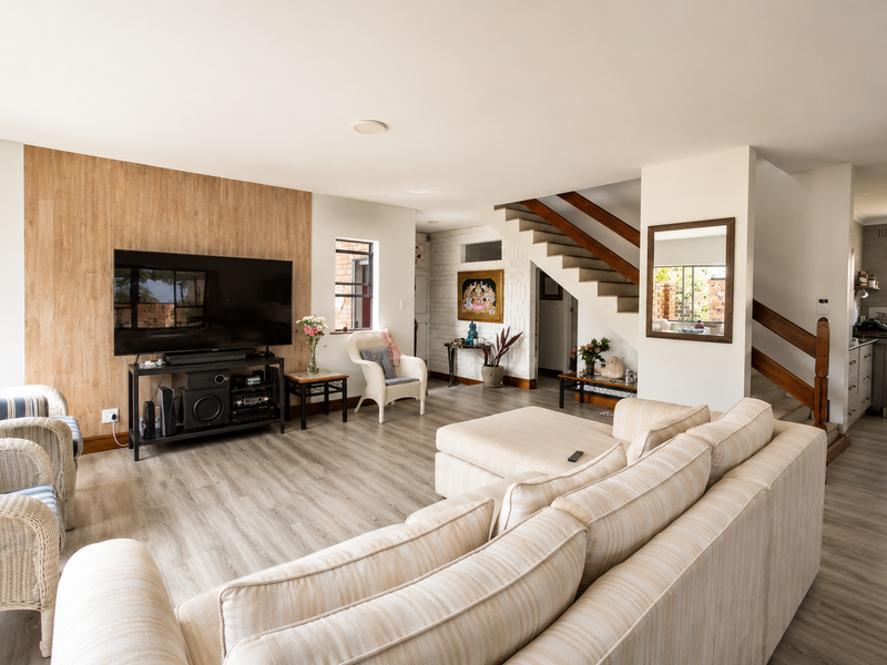 Spacious open-plan living area featuring a timber accent wall, light wood-look flooring, and a staircase with a wooden handrail.