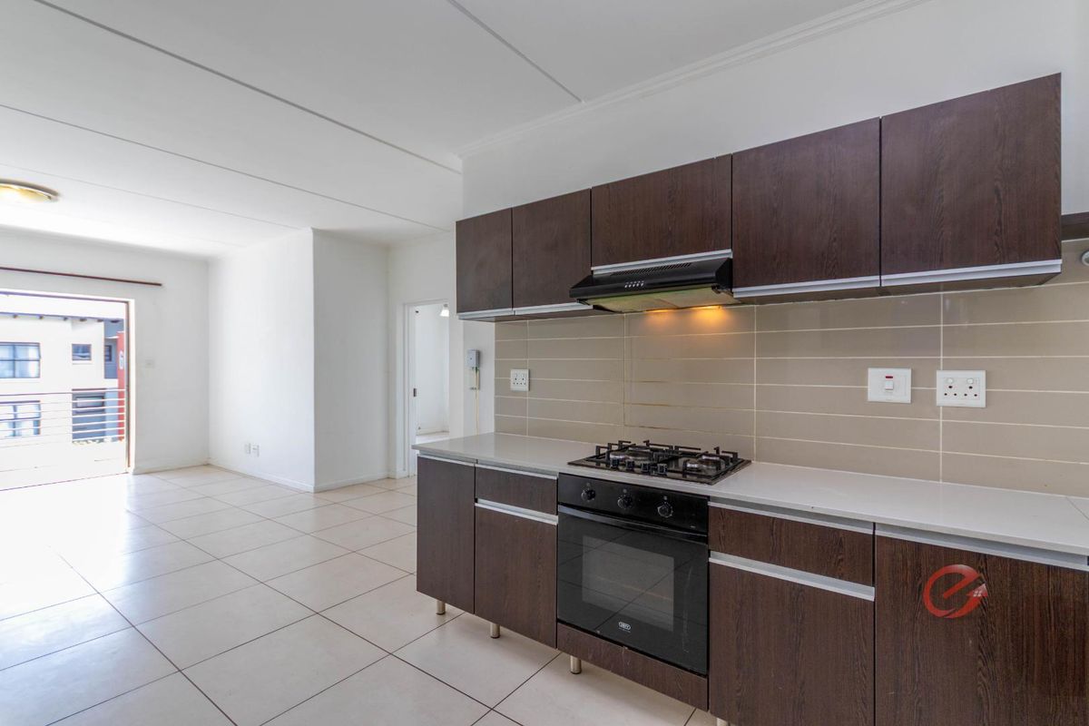 Modern kitchen featuring dark wood cabinetry, stone countertops, built-in oven, gas hob, and extractor fan, seamlessly flowing into an open-plan living area.