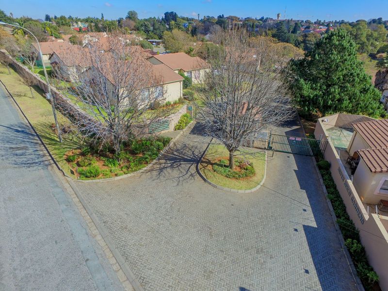 Aerial view of the townhouse complex entrance, featuring a paved driveway, secure gated access, and established garden landscaping.