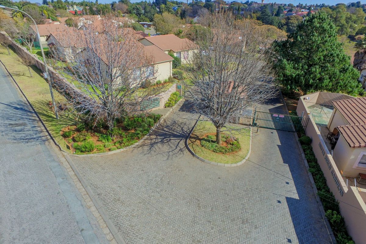 Aerial view of the townhouse complex entrance, featuring a paved driveway, secure gated access, and established garden landscaping.