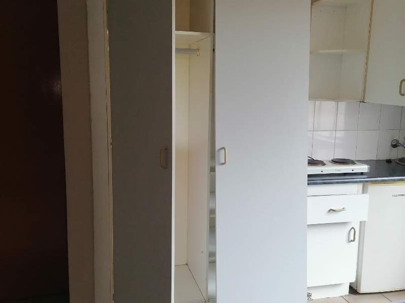 A compact kitchen area featuring built-in cabinetry, tiled flooring, and a basic hob, showing signs of wear and requiring cosmetic updates.
