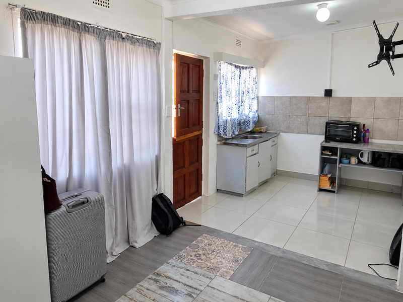 Open-plan living area featuring tiled flooring, a functional kitchen kitchenette with cabinetry, and direct access to an exterior timber door.