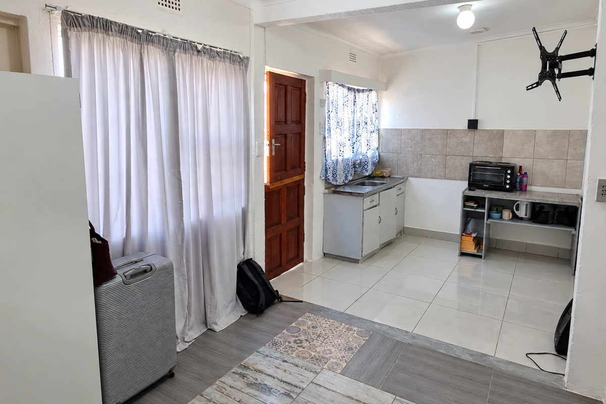 Open-plan living area featuring tiled flooring, a functional kitchen kitchenette with cabinetry, and direct access to an exterior timber door.