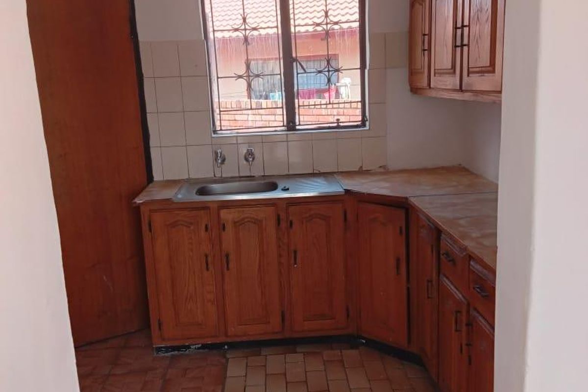 A dated kitchen featuring wooden cabinetry, a stainless steel sink, and tiled flooring, offering a functional space ready for modernization.