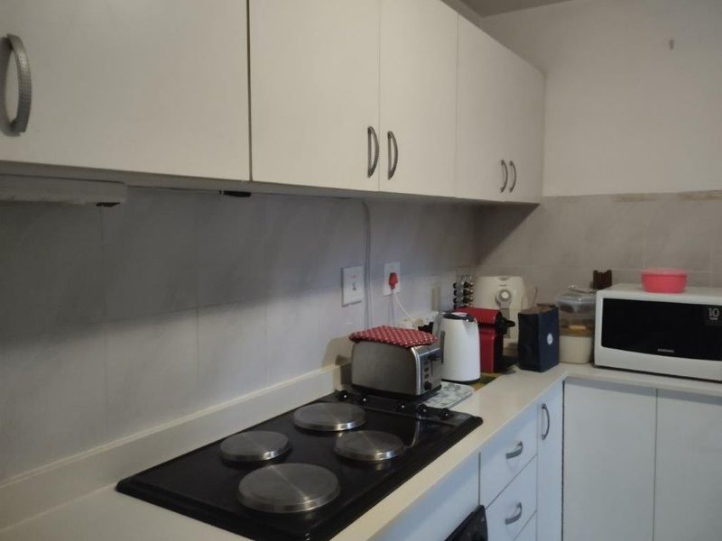 A functional kitchen featuring white built-in cabinetry, a black electric hob, and a tiled backsplash, offering a clean and practical workspace.