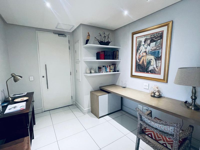 A functional home office space featuring a built-in desk, integrated shelving, recessed lighting, and clean tiled flooring.