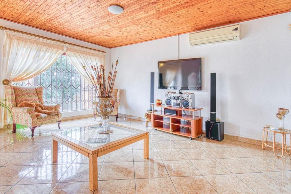 A spacious living room featuring tiled flooring, a timber-clad ceiling, and a wall-mounted air conditioning unit.