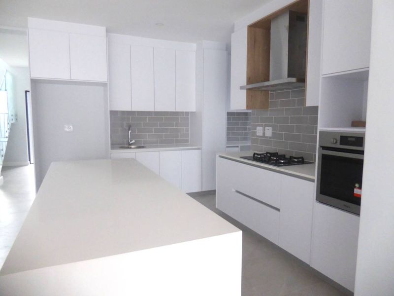 Modern kitchen featuring white cabinetry, stone countertops, a central island, subway tile backsplash, and integrated stainless steel appliances.