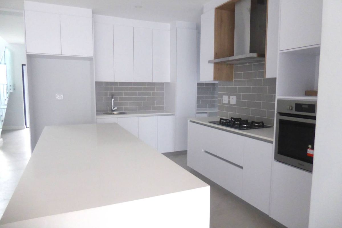 Modern kitchen featuring white cabinetry, stone countertops, a central island, subway tile backsplash, and integrated stainless steel appliances.