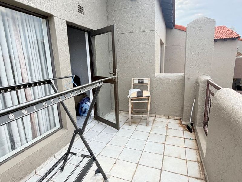 A private balcony featuring tiled flooring, plastered walls, and a metal balustrade, offering a functional outdoor space for the apartment.