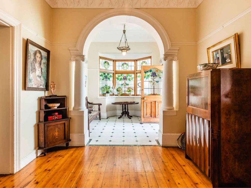Elegant entrance hall featuring polished timber floors, a grand arched entryway with columns, and beautiful stained glass windows.