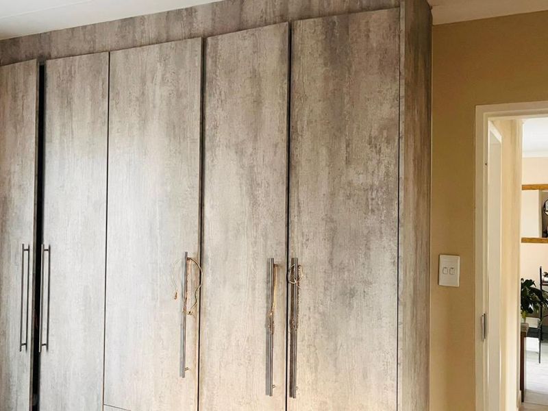 A bedroom featuring modern, wood-look built-in cupboards with sleek vertical handles, providing ample storage space.