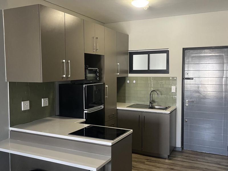 Modern kitchen featuring sleek grey cabinetry, stone-look countertops, integrated oven and hob, and a stylish olive green tiled splashback.