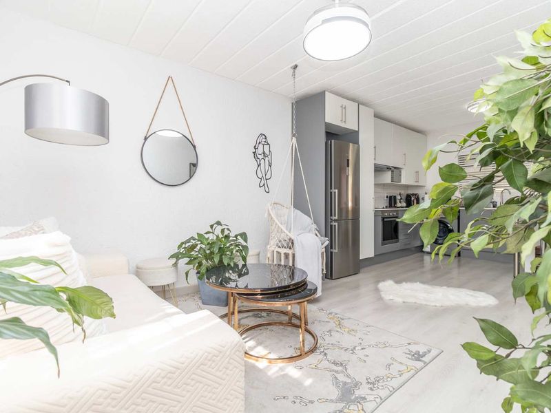 A bright open-plan living area featuring a modern kitchen with built-in cabinetry, integrated appliances, and light-toned laminate flooring throughout.