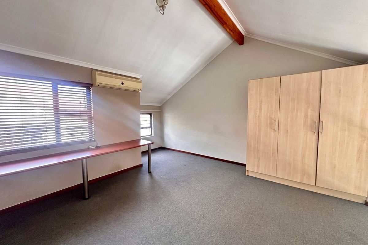 Spacious bedroom featuring vaulted ceilings with exposed timber beams, built-in cabinetry, a fitted desk, and an integrated air conditioning unit.