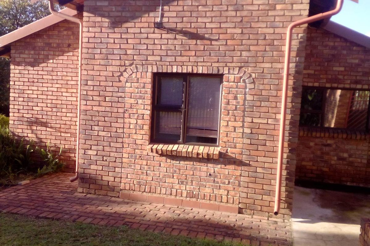 A view of the rear exterior brick facade featuring a window with dark frames, brick paving, and integrated downpipes.