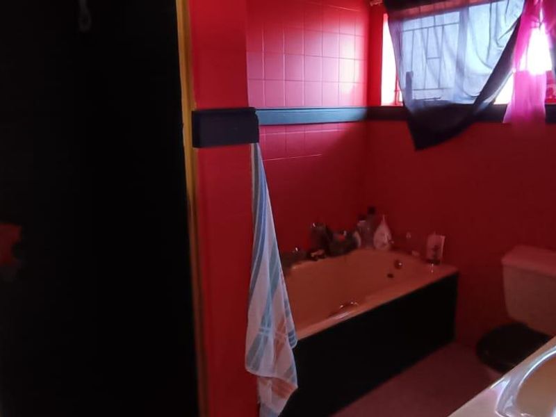 A dated bathroom featuring a bathtub, pedestal basin, toilet, and shower enclosure with bold red wall tiling.