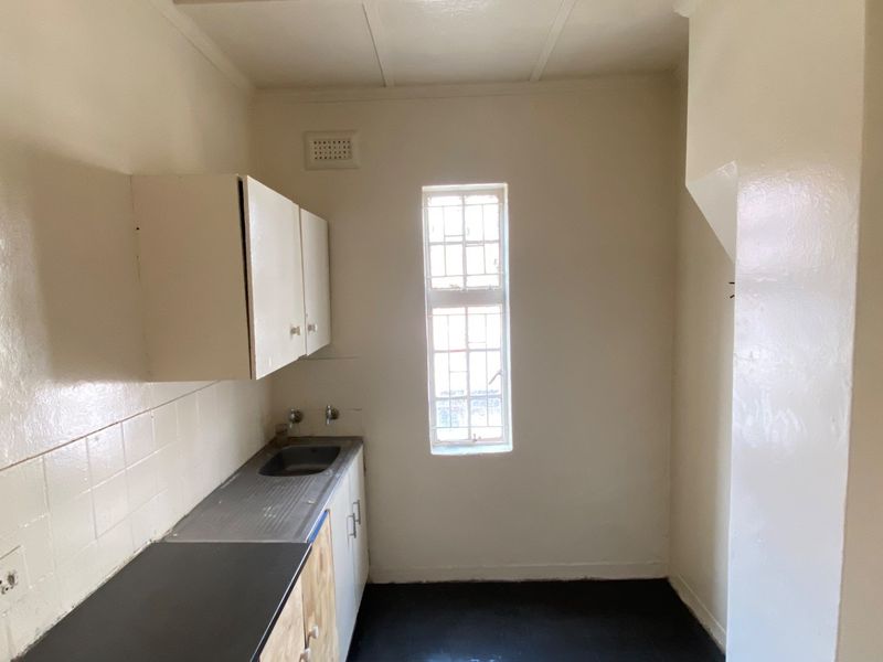 A compact, empty kitchen area featuring basic built-in cabinetry, a stainless steel sink, and tiled splashback, offering a blank canvas for renovation.
