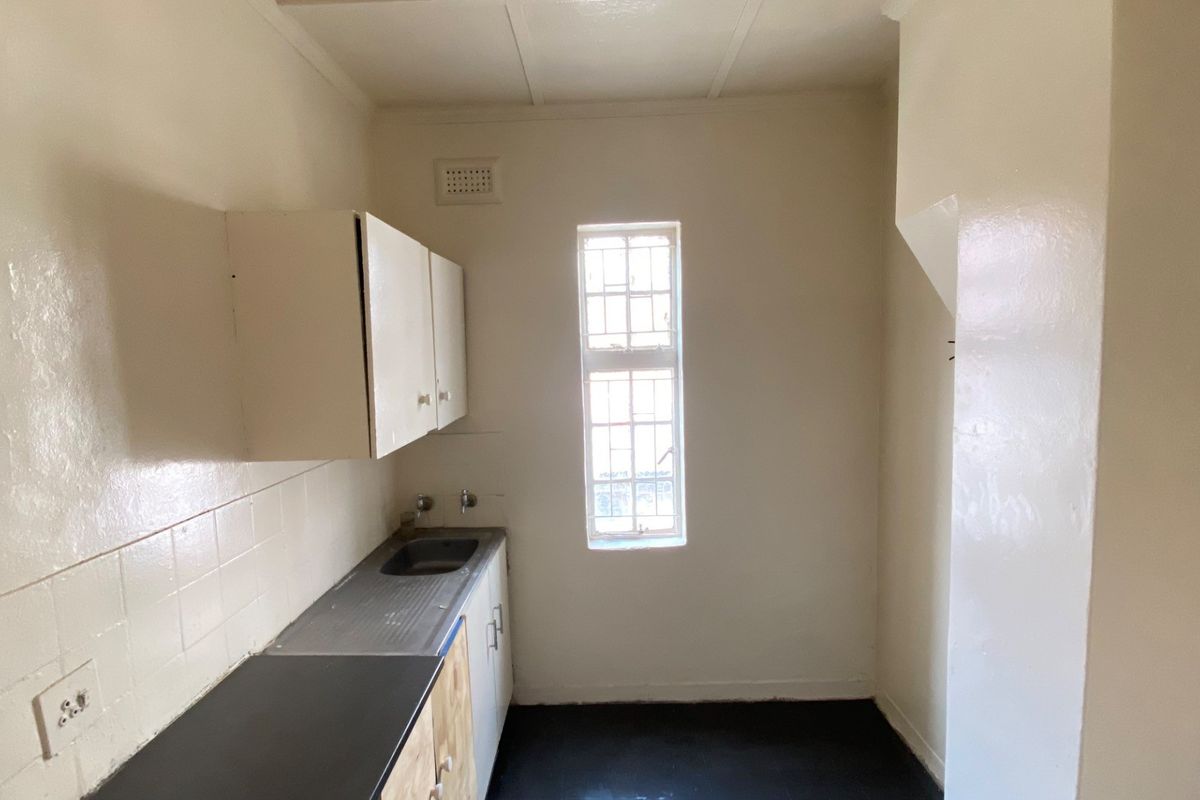 A compact, empty kitchen area featuring basic built-in cabinetry, a stainless steel sink, and tiled splashback, offering a blank canvas for renovation.