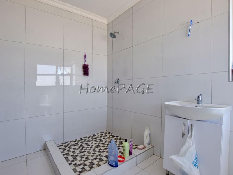 A functional bathroom featuring a tiled shower enclosure, a modern vanity cabinet with a wash basin, and full-height wall tiling.